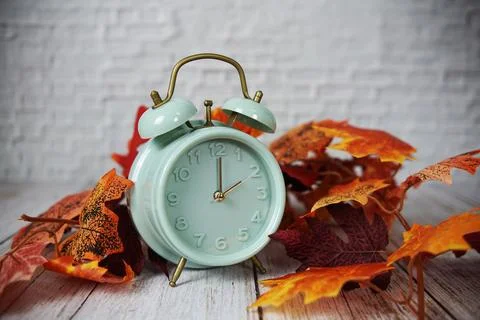 Alarm clock and maple lef on wooden bacground Stock Photos