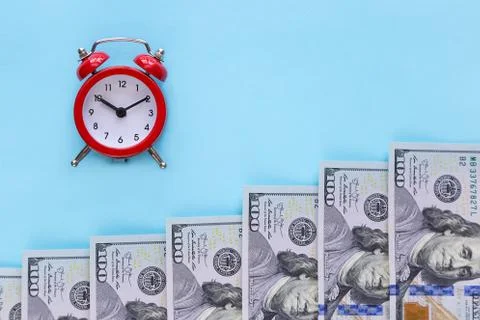 The alarm clock and a stack of money on a blue background Stock Photos