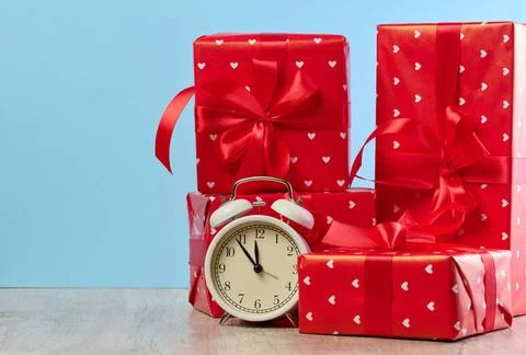 Alarm clock and stack of red gift boxes on blue background Alarm clock and... Stock Photos
