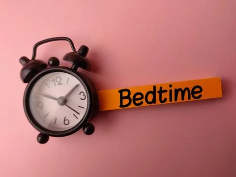 Alarm clock and sticky note with the word Bedtime on a pink background Stock Photos