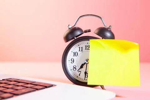 Alarm clock and yellow post it note on pink background with copy space Stock Photos