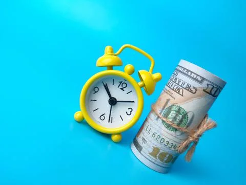 Alarm clock with banknotes on blue background with copy space. Stock Photos