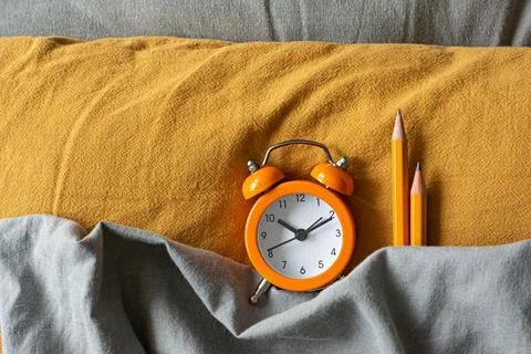 Alarm clock in bed on colored textiles. The concept of awakening, work time Stock Photos