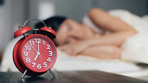 The alarm clock on a bedside table against the background of the sleeping woman Stock Footage 127320104