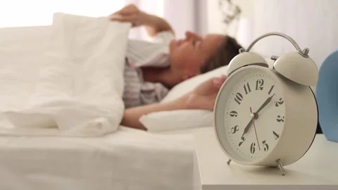 Alarm clock on bedside table as cute woman wakes up. Greet morning with scene of Stock Footage 275441195