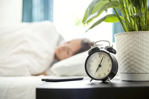 Alarm clock on bedside table going to ring early morning to wake up woman Stock Photos