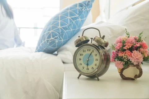 Alarm clock on the bedside table with a pink flower vase beside in the bedroo Stock Photos