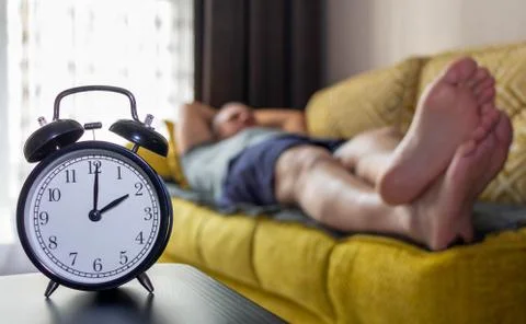 Alarm clock close-up on a background of a sleeping man. Stock Photos