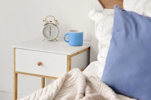 Alarm clock with cup on bedside table in light room Stock Photos