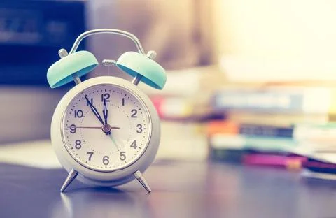 Alarm clock on the desk, books and office stuff in the blurry background, ... Stock Photos