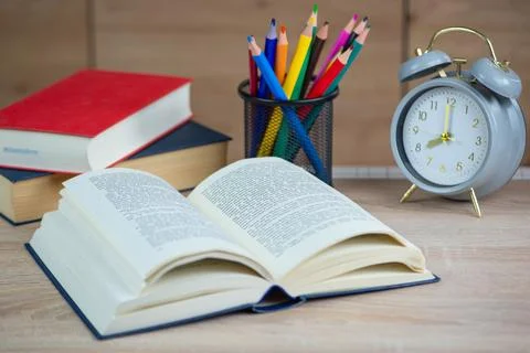 Alarm clock on the desk to read Open book in the background selective focus.. Stock Photos