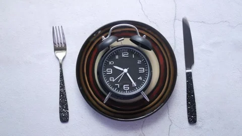 Alarm clock on dinner plate with fork and knife shows passing time. Stock Footage 332623324