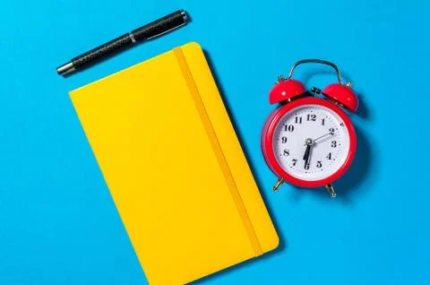 Alarm clock, empty notebook on blue background. Stock Photos