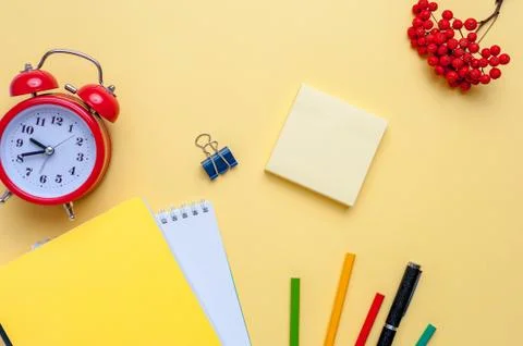 Alarm clock, empty notebook, pencils on yellow background. Stock Photos