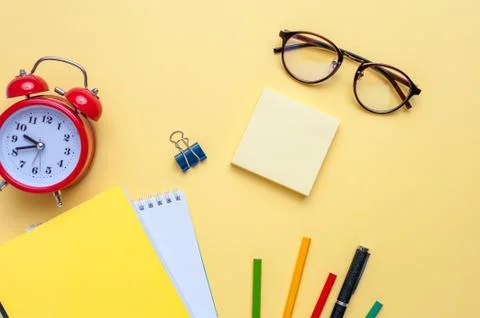 Alarm clock, empty notebook, pencils on yellow background. Stock Photos