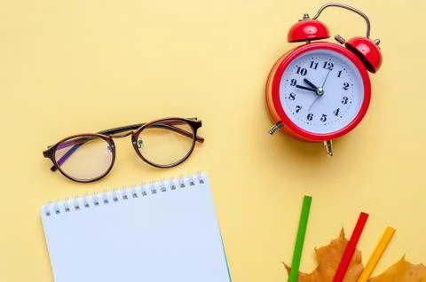 Alarm clock, empty notebook, pencils on yellow background. Stock Photos