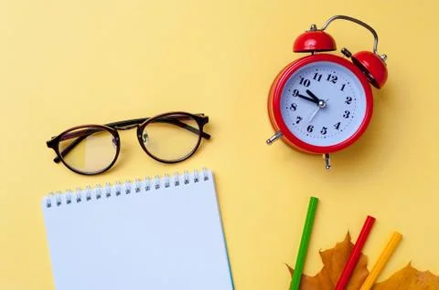 Alarm clock, empty notebook, pencils on yellow background. Stock Photos