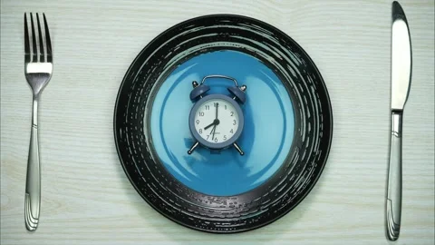 An alarm clock on an empty plate with fork and knife in the white table. StopMo Video stock 273995446
