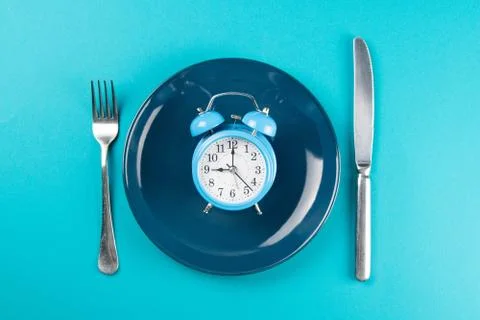 Alarm clock with fork and knife on the blue plate on blue table. Time to eat, Foto stock