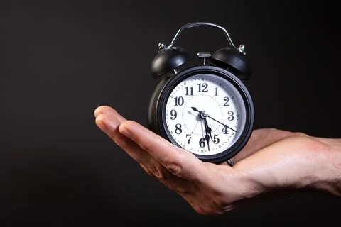 Alarm clock in hand on black background. Time management concept. Stock Photos