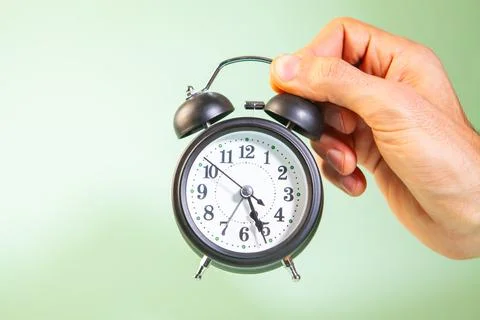 Alarm clock in hand on green background. Time management concept. Stock Photos