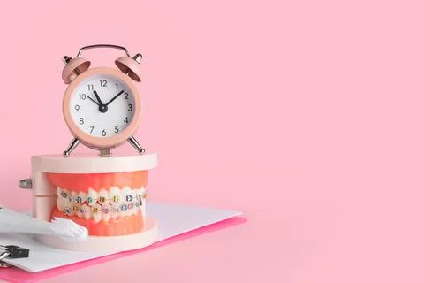Alarm clock, jaw model with braces, toothbrush and clipboard on pink backgrou 스톡 사진