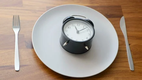 The alarm clock lies on an empty plate, kurpny plan. Concept: cooking, diet Stock Footage 128254026