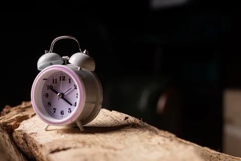 Alarm clock on log on dark background. Concept of time management. Circadia.. Stock Photos
