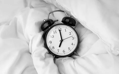 Alarm clock lying on white bed Stock Photos