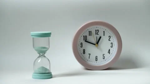Alarm clock with minutes move fast and hourglass with flowing sand on white back Stock Footage 219609727