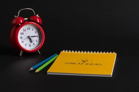 Alarm clock with notepad and colored pencils on black background, isolated... Stock Photos