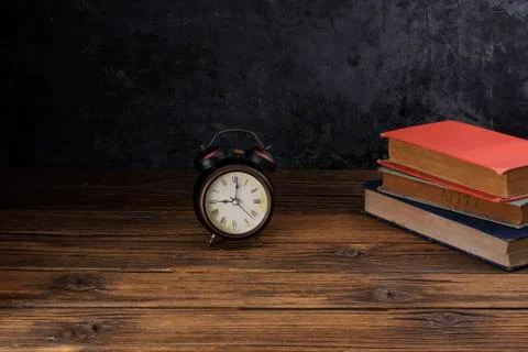Alarm clock placed on old books on old wooden table black wall background Stock Photos