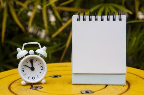 Alarm clock pointing at 10 o'clock with blank notepad. Blurred park backgro.. Stock Photos