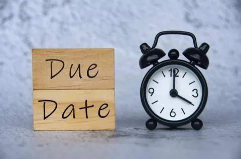 Alarm clock pointing at 4 o'clock with text on wooden block - Due Date. Stock Photos