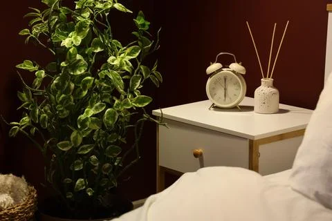 Alarm clock with reed diffuser on nightstand in dark bedroom Stock Photos