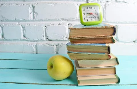 Alarm clock on  stack of old books, apple against a white brick wall. School  Stock Photos