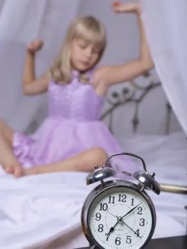 Alarm clock standing on bedside table. Wake up of an asleep young girl is 스톡 사진