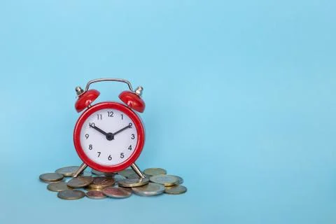 The alarm clock stands on a stack of money on a blue background Stock Photos