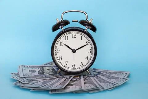 The alarm clock stands on a stack of money on a blue background Stock Photos