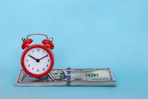 The alarm clock stands on a stack of money on a blue background Stock Photos