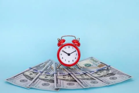 The alarm clock stands on a stack of money on a blue background Stock Photos