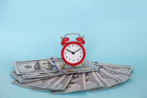 The alarm clock stands on a stack of money on a blue background Stock Photos