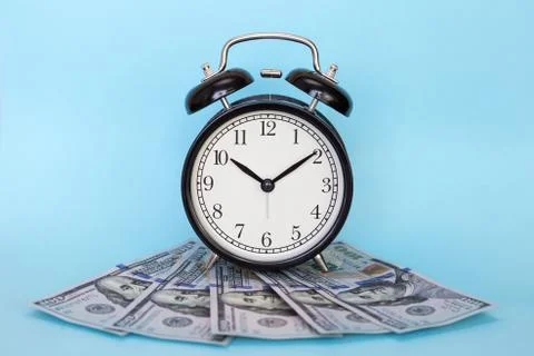 The alarm clock stands on a stack of money on a blue background Stock Photos