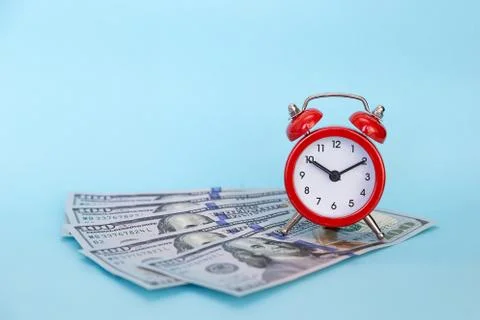 The alarm clock stands on a stack of money on a blue background Stock Photos