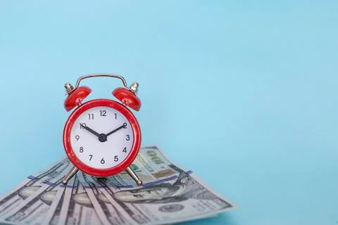 The alarm clock stands on a stack of money on a blue background Stock Photos