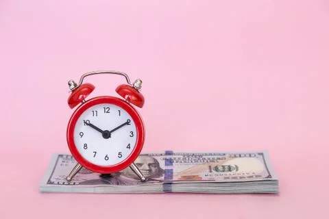 The alarm clock stands on a stack of money on a pink background Stock Photos