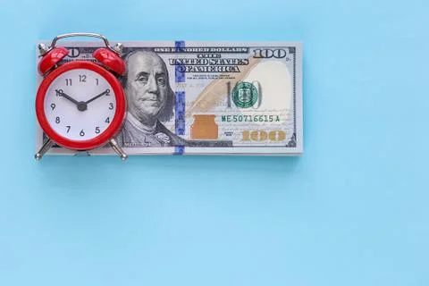 The alarm clock stands on a stack of money on a blue background Stock Photos
