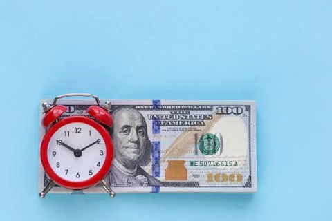 The alarm clock stands on a stack of money on a blue background Stock Photos