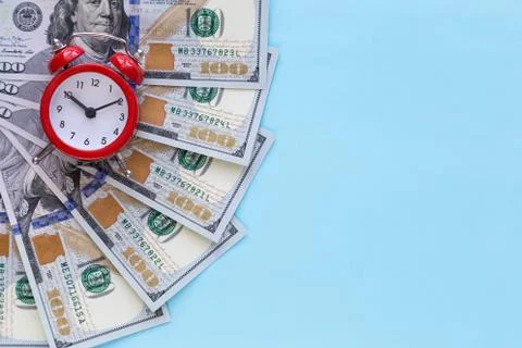 The alarm clock stands on a stack of money on a blue background Stock Photos