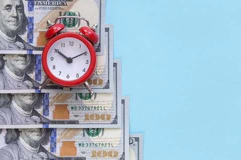 The alarm clock stands on a stack of money on a blue background Stock Photos
